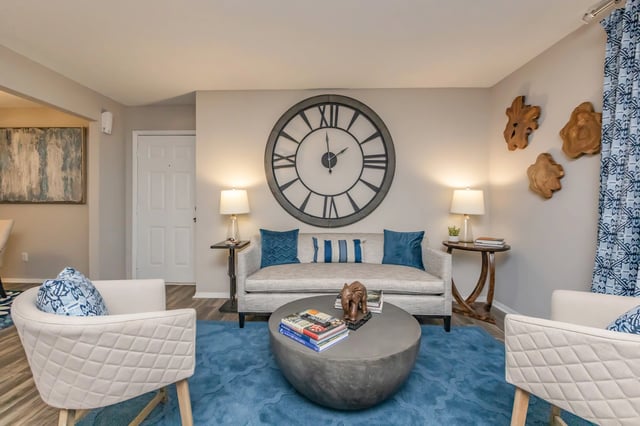 Living room with a large clock, sofa, two chairs, and blue rug.