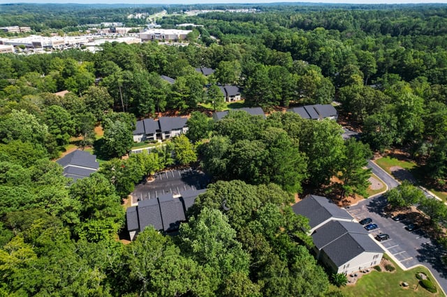 Aerial view of apartment buildings nestled among lush green trees with a parking lot.