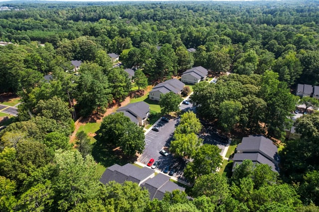 Aerial view of apartment buildings nestled among lush trees with a parking lot.