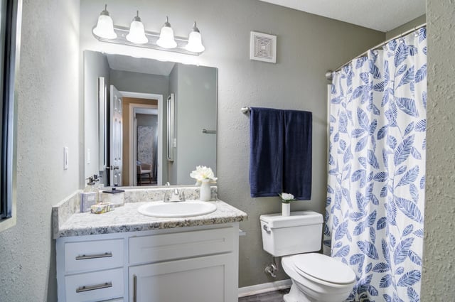 Bathroom with vanity, toilet, and shower with blue leaf pattern curtain.