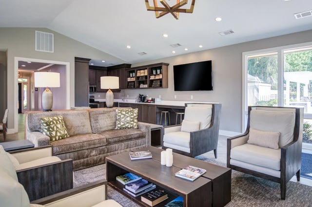 Modern lounge area with comfortable seating, a large TV, and a small kitchenette.