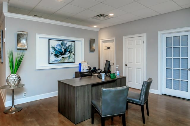 Front desk area with a wooden desk, two chairs, and artwork on the wall.