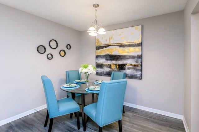 Dining room with a round glass table, four blue chairs, and modern artwork.
