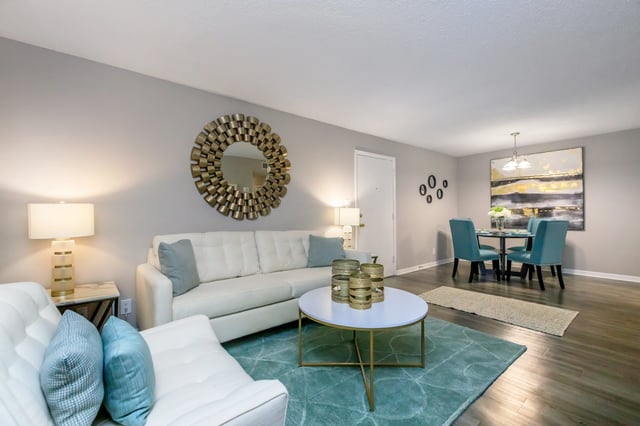 A staged living room and dining area with white sofas, teal dining chairs, and modern decor.