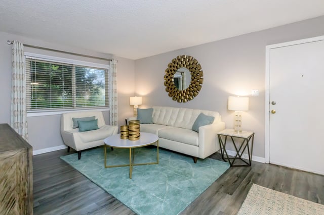 A living room featuring a white sofa, armchair, coffee table, and a large decorative mirror.