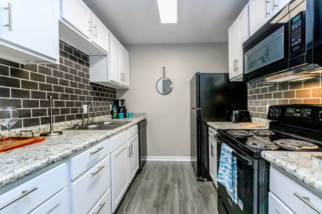 Modern kitchen with white cabinets, black subway tile backsplash, and granite countertops.