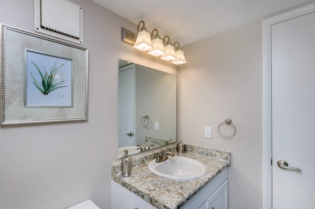 Bathroom vanity with granite countertop, sink, faucet, mirror, and light fixture. Includes framed artwork.