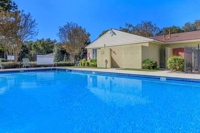 Sparkling blue swimming pool with a building and trees in the background.