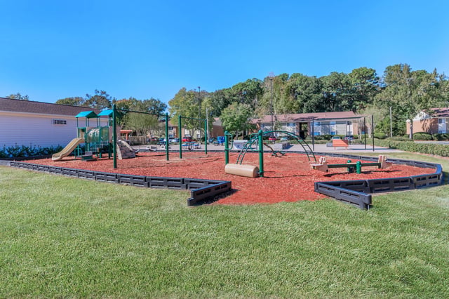 Playground with swings, slides, and climbing structures in front of apartment buildings.