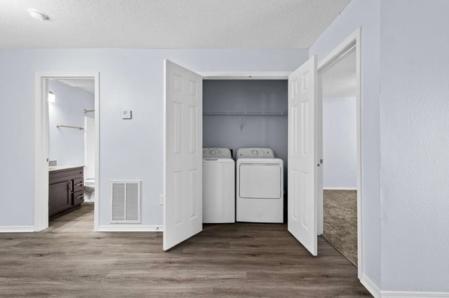 Washer and dryer inside a closet. A bathroom is visible through an open doorway to the left.