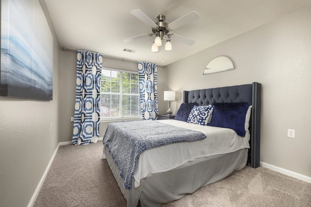 Bedroom with a queen-size bed, navy blue tufted headboard, and patterned curtains.