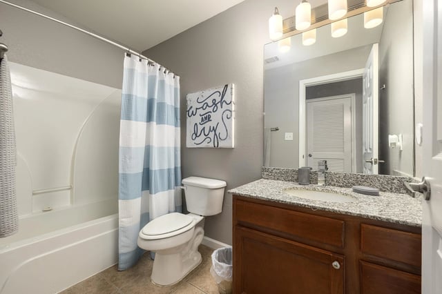 Bathroom with a bathtub, toilet, and vanity with a granite countertop.