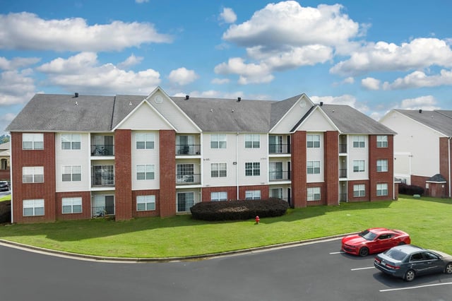 Exterior of apartment building with red brick and white siding, balconies, and parking lot.
