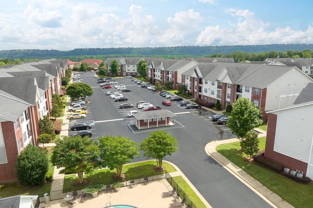 Aerial view of apartment buildings with a large parking lot and lush landscaping.