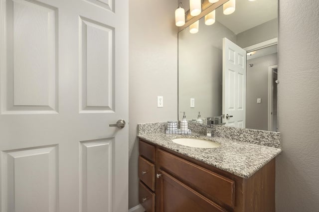Bathroom vanity with granite countertop, white sink, and modern light fixtures.