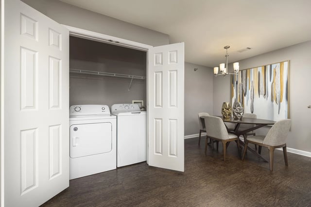 Washer and dryer in a closet next to a dining area with a table and chairs.