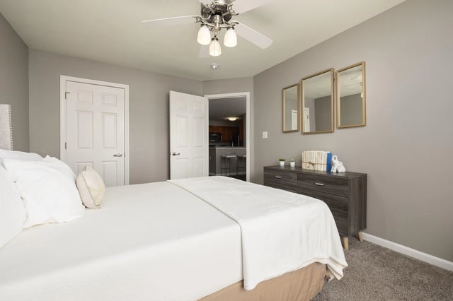 Cozy bedroom with a king-size bed, white linens, a ceiling fan, and a dresser with decorative items.