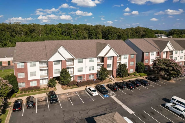 Aerial view of apartment buildings with parking lot and trees.