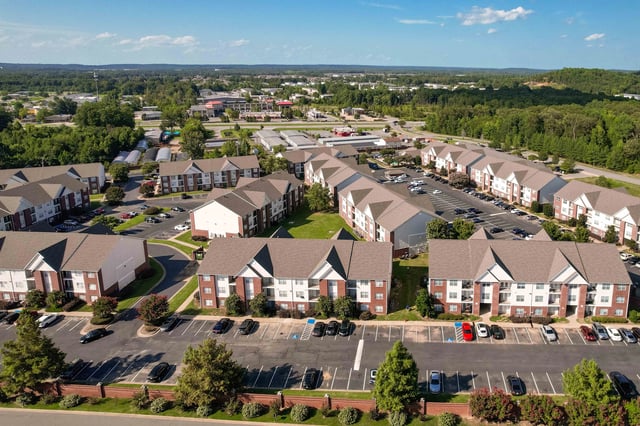 Aerial view of apartment buildings with parking lots and surrounding landscape.