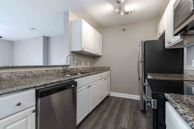 Kitchen featuring granite countertops, white cabinets, stainless steel dishwasher, and refrigerator.