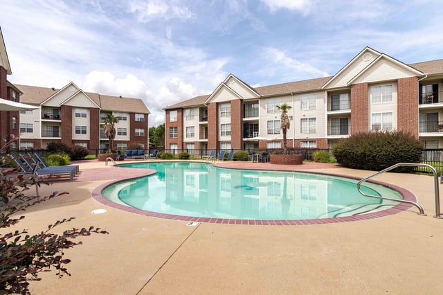 Resort-style swimming pool with lounge chairs and apartment buildings in the background.