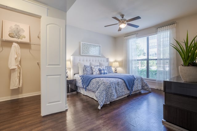 Luxurious bedroom with king-size bed, blue and white bedding, walk-in closet, and a ceiling fan.