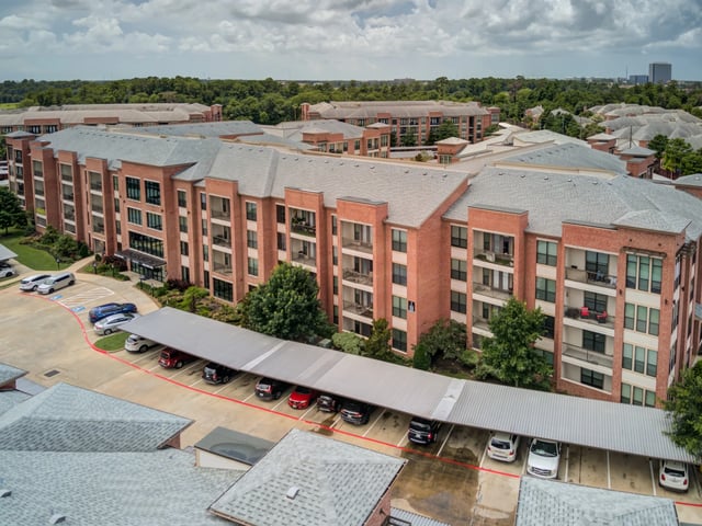 Aerial view of a brick apartment building with covered parking and surrounding trees.