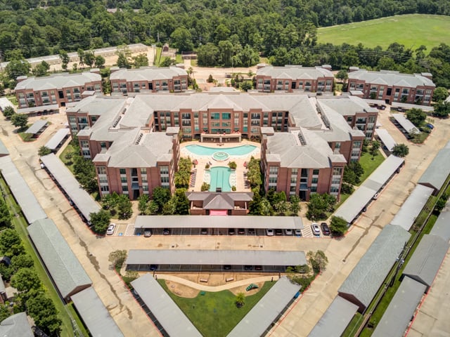 Aerial view of apartment buildings with a courtyard pool and surrounding parking.