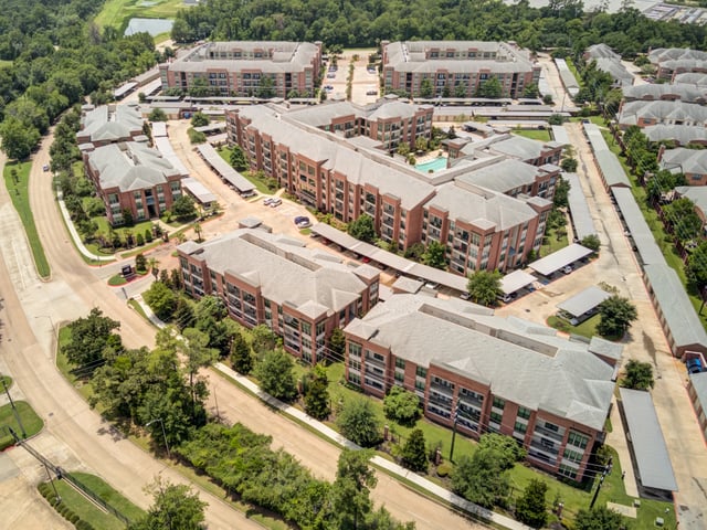 Aerial view of apartment buildings with covered parking and a pool.