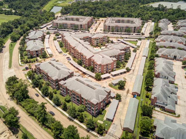 Aerial view of a large apartment complex with multiple buildings, parking garages, and lush landscaping.