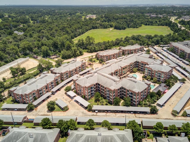 Aerial view of a multifamily apartment complex with U-shaped buildings surrounding a courtyard with a swimming pool.