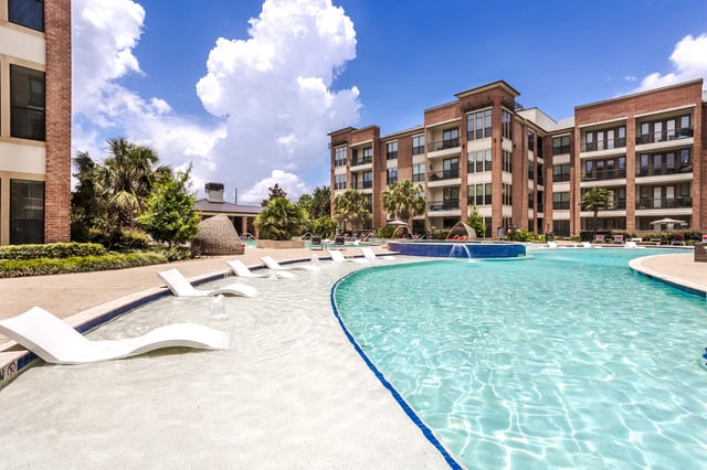 Modern apartment complex with a resort-style pool and lounge chairs.