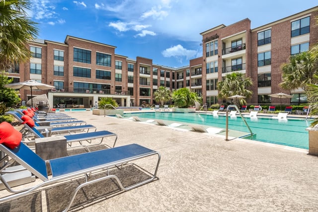 Outdoor swimming pool area with lounge chairs and a modern brick apartment building in the background.