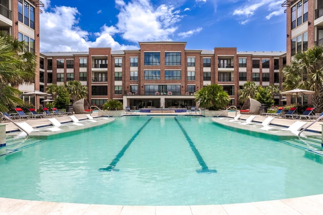 Resort-style swimming pool with lounge chairs and a modern apartment building in the background.