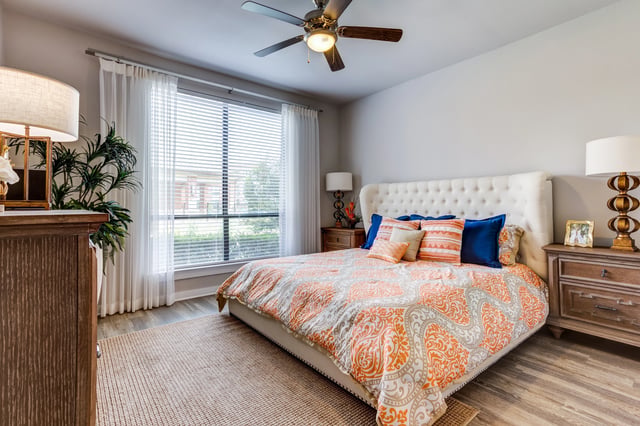 A king-sized bed with orange and white patterned comforter and blue pillows in a bedroom with a ceiling fan.