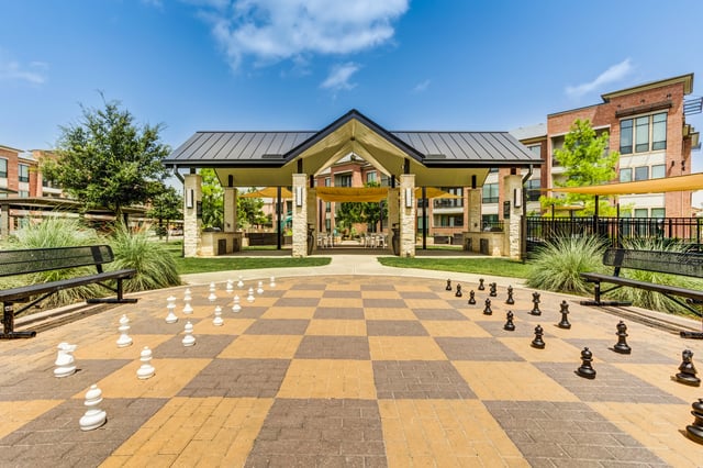 Outdoor oversized chess board with benches and covered seating area in the background.