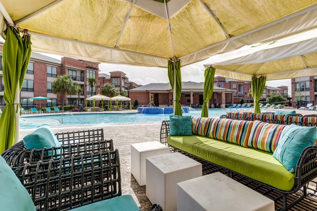 Cabana seating area overlooking a swimming pool and apartment buildings.