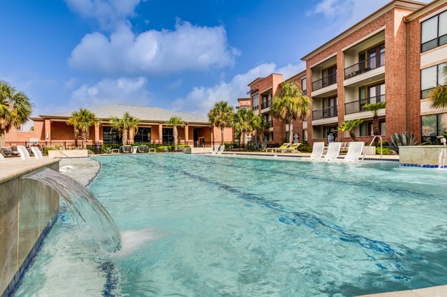 Resort-style swimming pool with lounge chairs and palm trees.