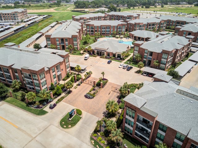 Aerial view of a large apartment complex with multiple buildings, a pool, and parking areas.