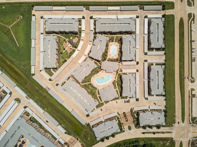 Aerial view of a multifamily property with multiple buildings, a pool, and parking areas.