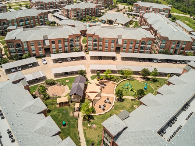 Aerial view of apartment complex buildings, parking, and community amenities including a playground and courtyard.