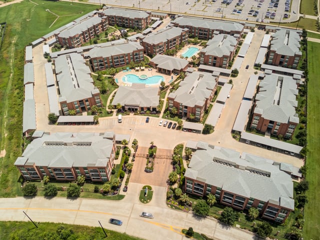Aerial view of a large apartment complex with multiple buildings, a pool, and parking.