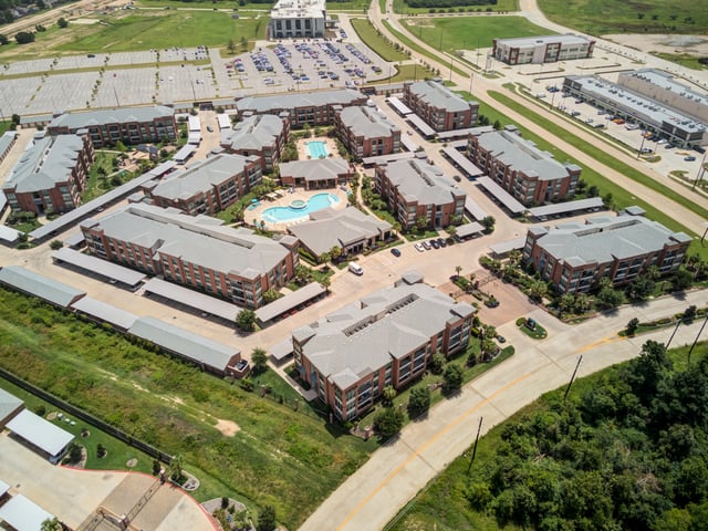 Aerial view of a multifamily property featuring apartment buildings, a swimming pool, and covered parking.