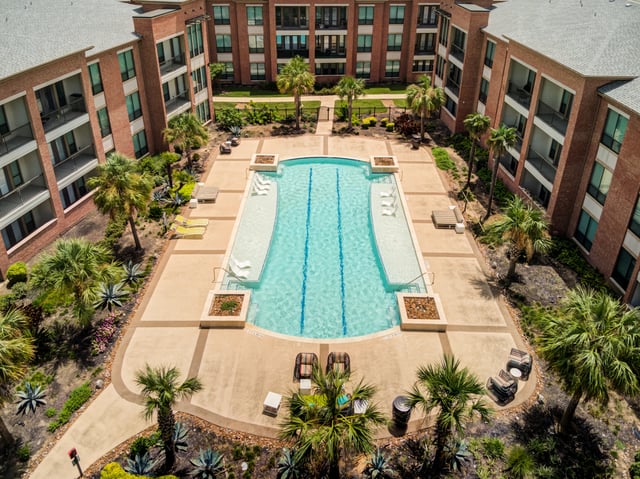 Aerial view of a resort-style swimming pool with lounge chairs and palm trees at a multifamily property.