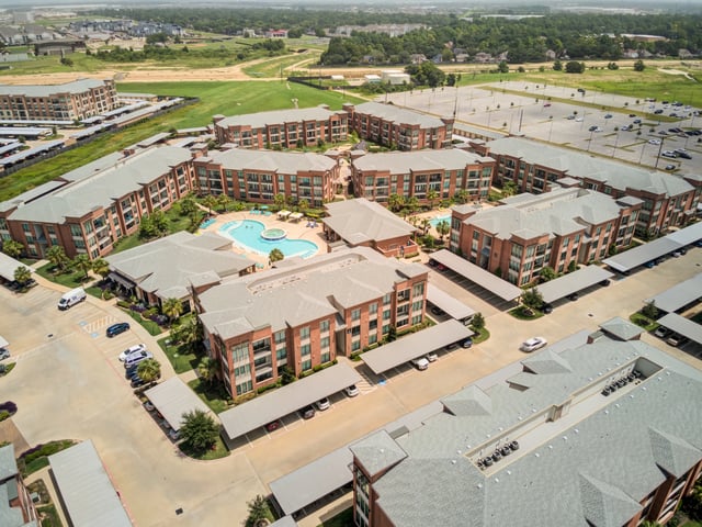 Aerial view of apartment complex buildings and amenities including a pool and parking.
