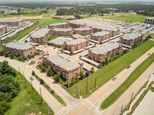 Aerial view of a multifamily apartment complex with red brick buildings, carports, and a swimming pool.