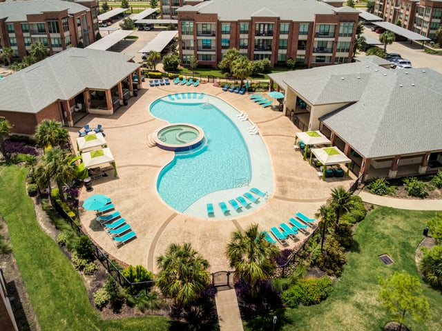 Aerial view of a resort-style swimming pool and hot tub area with lounge chairs and cabanas.