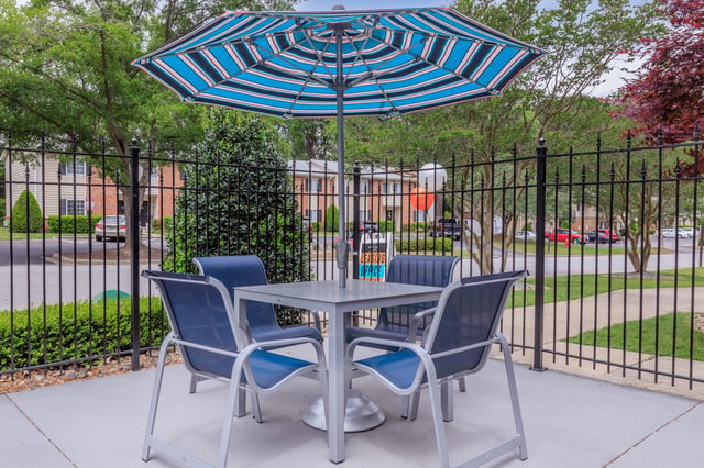 Outdoor seating area with table and chairs under a striped umbrella.