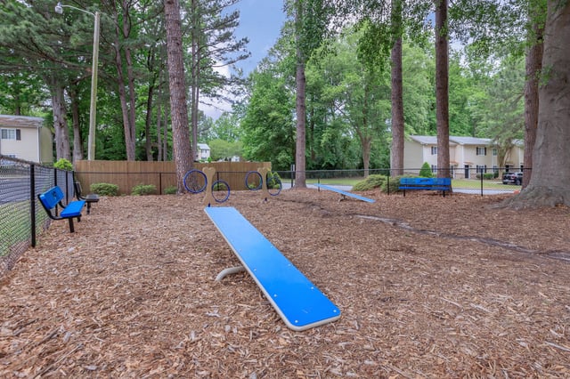 Dog park with agility equipment, benches, and trees.