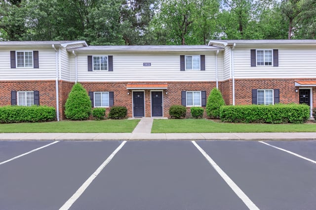 Exterior view of apartment buildings with brick and siding, manicured lawns, and parking spaces.